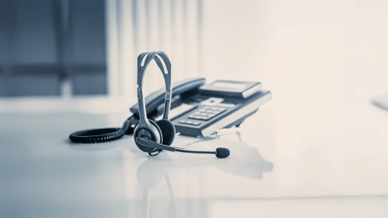Casque de support client posé devant un téléphone fixe sur un bureau.